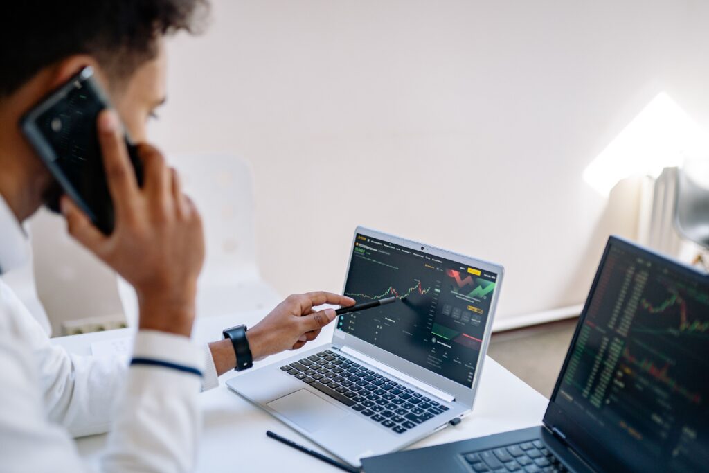 Business professional talking on phone and analyzing financial charts on laptops in office setting.